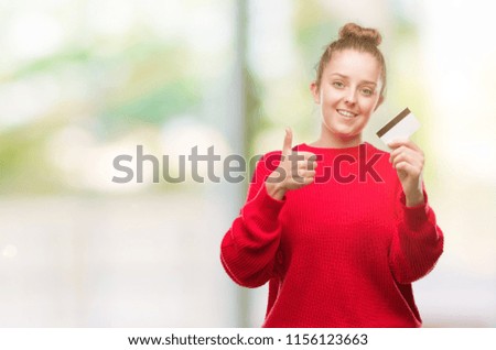 Young blonde woman holding credit card happy with big smile doing ok sign, thumb up with fingers, excellent sign