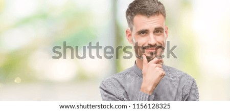 Young hipster man looking confident at the camera with smile with crossed arms and hand raised on chin. Thinking positive.
