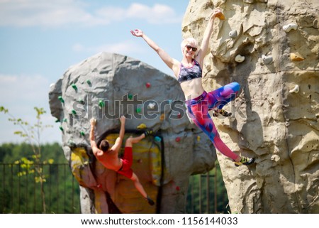 Photo of sports man and smiling woman in sunglasses climbing on boulders for rock climbing against blue sky with clouds