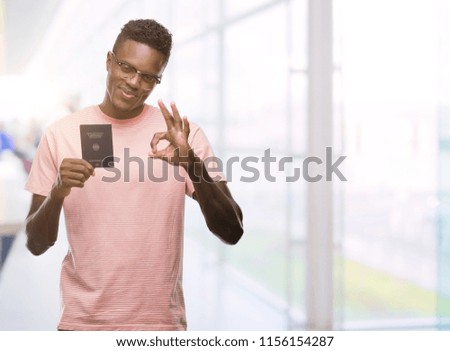Young african american man holding german passport doing ok sign with fingers, excellent symbol