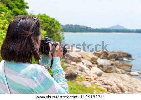 Young woman was happy to photography with dslr camera on the rock near the sea under the summer sky at Koh Samui island, Surat Thani province, Thailand