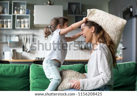 Mommy and kid daughter having pillow fight together, young babysitter nanny playing funny game with kid girl at home, happy mother and child enjoy spending time together, family leisure fun activity Royalty-Free Stock Photo #1156208425