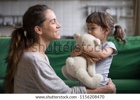 Smiling mother hugging cute little girl holding teddy bear toy showing love and care in family, young mom embracing protecting child, sincere relationships between mum and daughter cuddling concept Royalty-Free Stock Photo #1156208470
