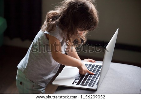 Curious smart little girl typing on laptop alone, clever cute child using computer online without permission, forbidden internet content parental protection, pc control and security for kid concept Royalty-Free Stock Photo #1156209052