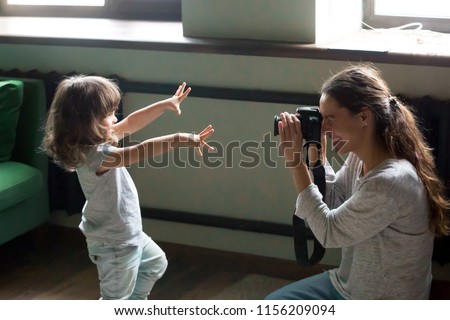 Mom photographer having fun playing making photo of artistic cute kid daughter at home, young mother photographing little child girl or shooting video on digital camera, funny family photo session
