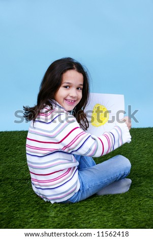Young girl sitting in the grass holding a picture of the sun