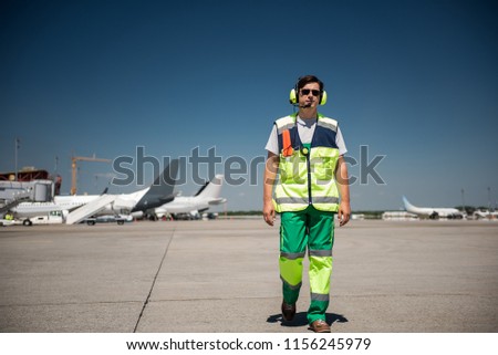 I am coming. Full length portrait of aviation marshaller walking down the runway. Man wearing sunglasses and headphones