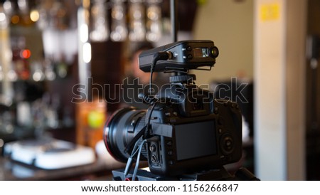 A camera on a tripod with a connected microphone records a video interview in a cafe