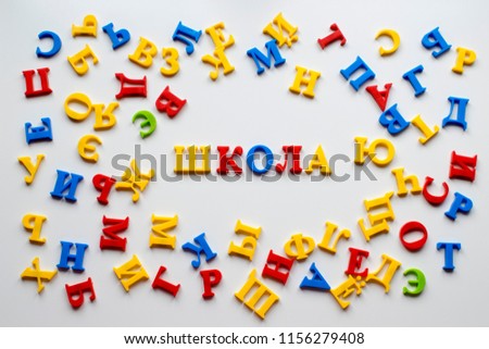 The word "school" of Russian letters among the letters of the Russian alphabet. Magnet letters on a white magnetic board and school inscription, background image, Cyrillic alphabet