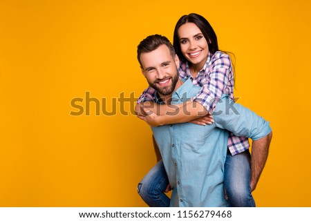 Portrait with copyspace of stylish trendy couple, handsome man carrying on back beautiful woman with beaming smile isolated on bright yellow background