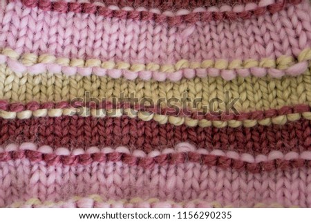 Close-up of a hand-knit winter hat in modern colors, beige, rose ash and cherry. Thick and warm woolen yarns suitable for cold winter days. Shallow depth of focus. Hobby concept.