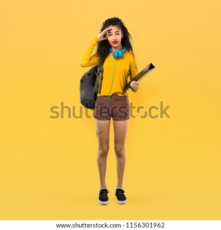 Full body of Teenager student girl with curly hair with surprise and shocked facial expression. Gaping because can not believe what is happening on yellow background