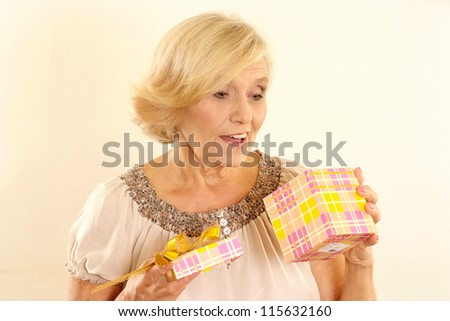portrait of happy beautiful old woman with a gift on the beige