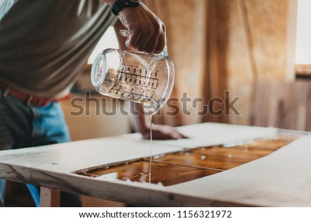 Detail of Skilled Artisan Carpenter Working on a Piece of Furniture with Epoxy Resin in his Workshop Royalty-Free Stock Photo #1156321972