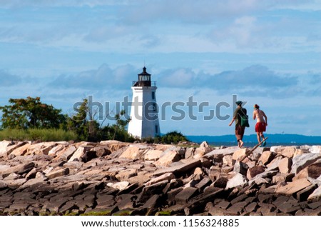 Two young hikers walking along jetty towards Black Rock Harbor lighthouse in Bridgeport, Connecticut. It is a popular park enjoyed by many visitors in the summer season. Royalty-Free Stock Photo #1156324885