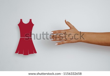 Top view of a woman's hand with pink tips reaches for a red dress, clothes. The concept of purchases, price reductions. Woman's hand on a gray, bright background. Shopping.