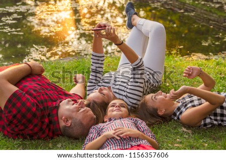 Happy family laying on green grass and take a selfie with mobile phone.Young family smiling in park by the lake at sunset.