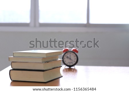 Books stacked on the desk. Alarm clock is the background selective focus and shallow depth of field