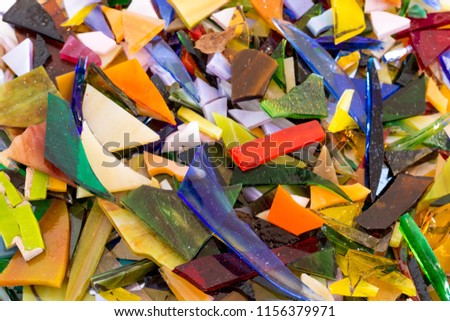 Close-up of bright multicolored stained glass chips in all shapes and sizes scattered and overlapping in a cheerful, shiny, unique background texture