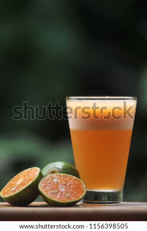 Picture of a glass of orange juice above wooden plate on blurred green leaf background. Selective focus