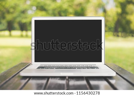 Laptop computer with blank black screen on green nature background. Natural and technology concept. Object and electronics theme. Front view angle
