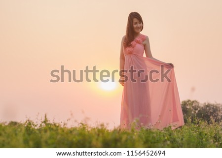 Portrait of happy asian woman wearing pink dress standing over sunset background.