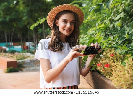 Smiling young girl making photos with camera at the park outdoors in summer