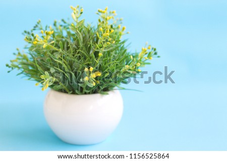 A green artificial imitated bush in a white ceramic pot placed on a bright blue background, leave free space on the right of frame.
