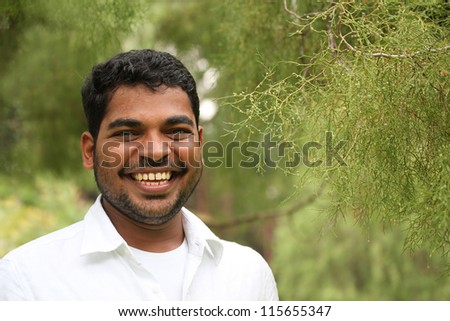 Close-up image of happy, excited & handsome asian/indian business-man with smiling expression. The person is wearing a white shirt & the picture is shot in natural settings