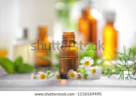 Bottle with essential oil and chamomile flowers on wooden table