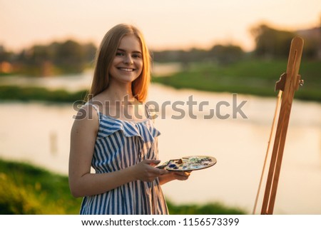 Sunset in park. blonde girl paints a painting on the canvas with the help of paints