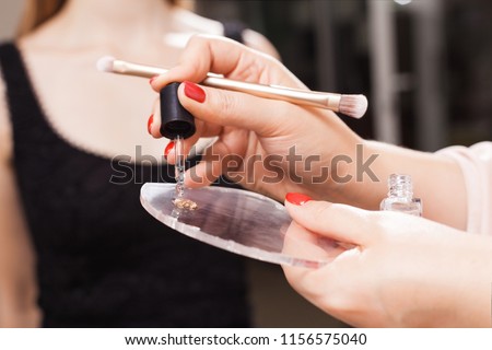 professional makeup artist mixing foundation and oil on a glassy surface before applying it on a face of a model. concept of natural make up Royalty-Free Stock Photo #1156575040