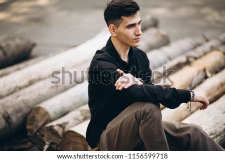 Young handsome man sitting on log in the park