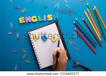 Word LEARN ENGLISH made with carved letters onyellow desk with office or school supplies, stationery. Concept of English language courses
