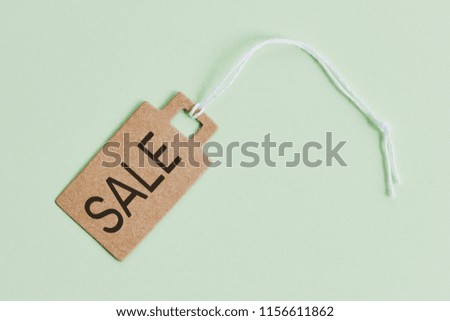 Brown cardboard price tag with sign sale on pastel green background, top view