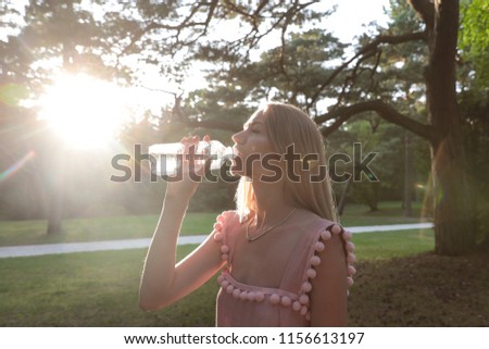 Beautiful young girl drinking water from a plastic bottle after a long walk in the woods