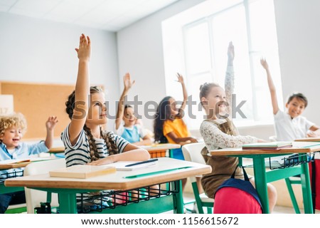 group of schoolchildren raising hands to answer question during lesson