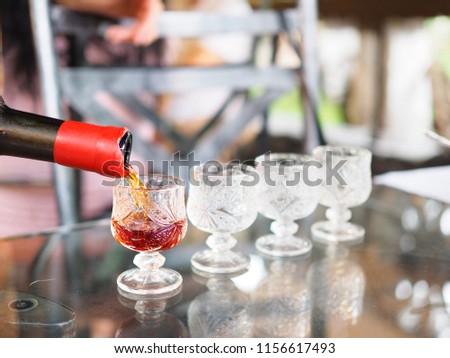 People pouring red wine into glasses in a row on table on blurred background for test drinking. Selective focus.