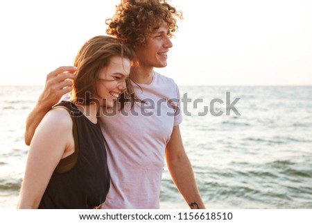 Picture of cute young loving couple walking outdoors on the beach.