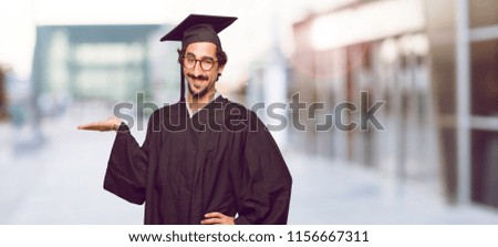 young graduated man smiling with a satisfied expression showing an object or concept with one hand and with the other hand on the hip.