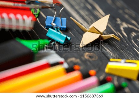 Origami on the background of the school stationery. Colored markers, sharpener and origami on a black background. Flat lay