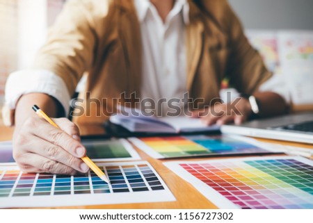 Young creative Graphic designer using graphics tablet to choosing Color swatch samples chart for selection coloring with work tools and accessories at workplace.