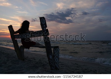      Girl silhouette sit on bench on beach in evening sunset with beautiful sky                                                       