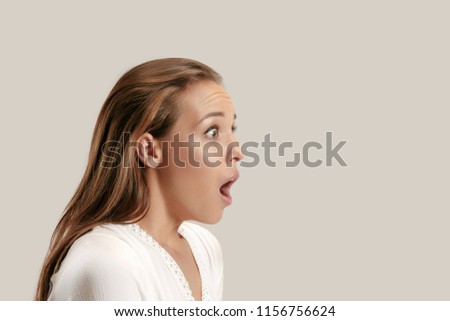 Wow. Beautiful female half-length profile portrait isolated on gray studio backgroud. Young emotional surprised woman standing with open mouth. Human emotions, facial expression concept.