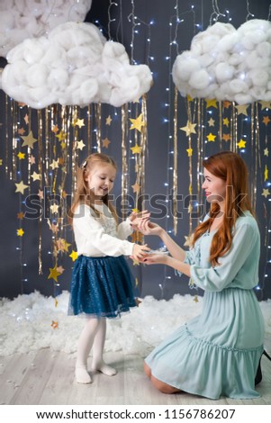 Happy little girl with a mom in a studio with a gold sparkling stars garland, fluffy clouds and lights. Magic christmas decor
