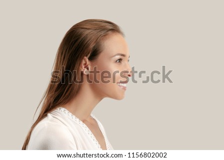 Happy business woman standing and smiling isolated on gray studio background. Beautiful female half-length portrait. Young emotional woman. The human emotions, facial expression concept. Profile view.