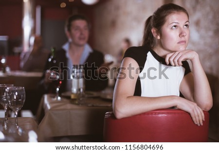 Portrait of offended young woman on background with drunk man at restaurant table