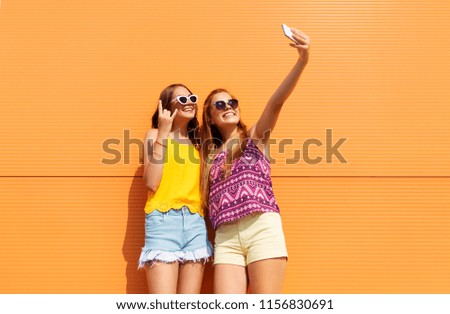 fashion, leisure and technology concept - smiling teenage girls taking selfie by smartphone and showing rock gesture outdoors in summer