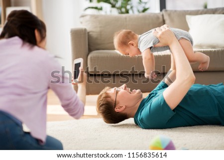 family, technology and people concept - happy mother and father taking picture or recording video of baby boy with smartphone at home
