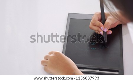 bright, soft shot of Asian little girl's right hand holding a plastic pen to draw a picture on black electronic pad at home in white background